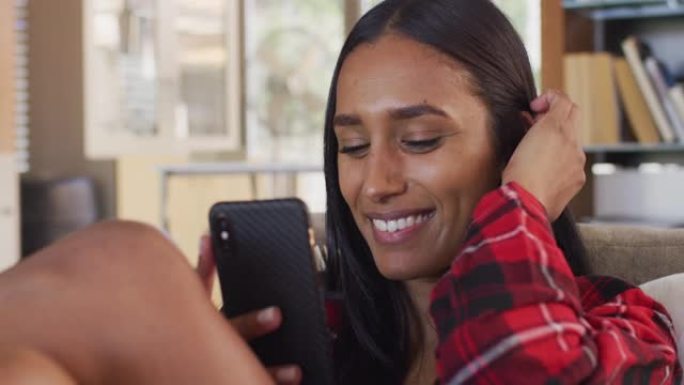 混合种族妇女使用智能手机，坐在沙发上进行视频对话