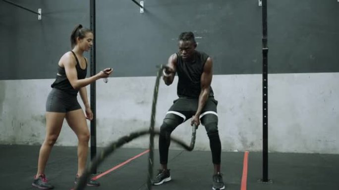 4k视频片段，一名年轻人在健身房与健身教练一起用战斗绳锻炼