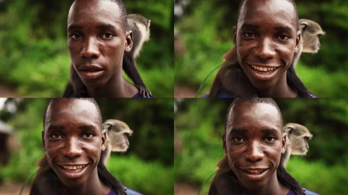 特写一位地地道道的非洲人看着相机，背着一只绿色的小猴子的肖像。黑人友好的男性微笑着享受着他村子里的大