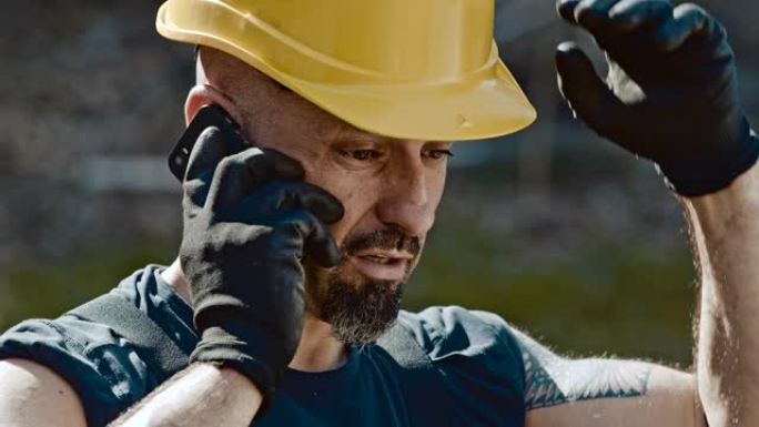 SLO MO建筑工人一边擦额头上的汗水一边用手机说话