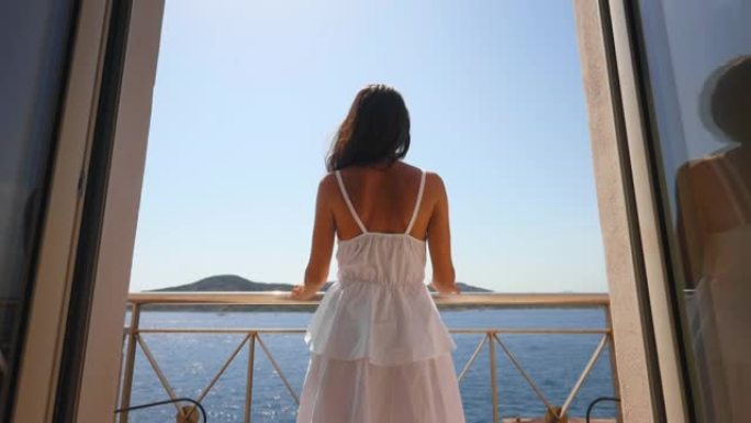 一名年轻女子的真实照片是在暑假假期旅行期间从酒店房间的露台上乘坐游艇在大海上欣赏全景。