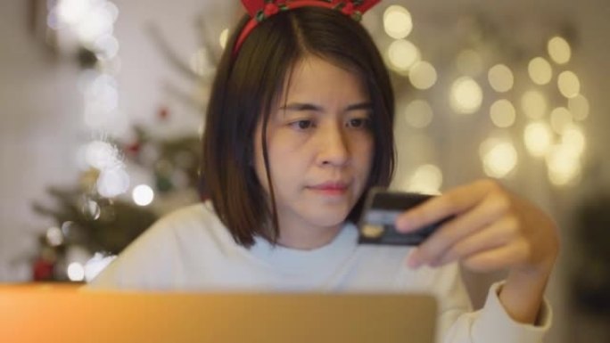 微笑的亚洲女性拿着笔记本电脑坐在家里买圣诞礼物。
