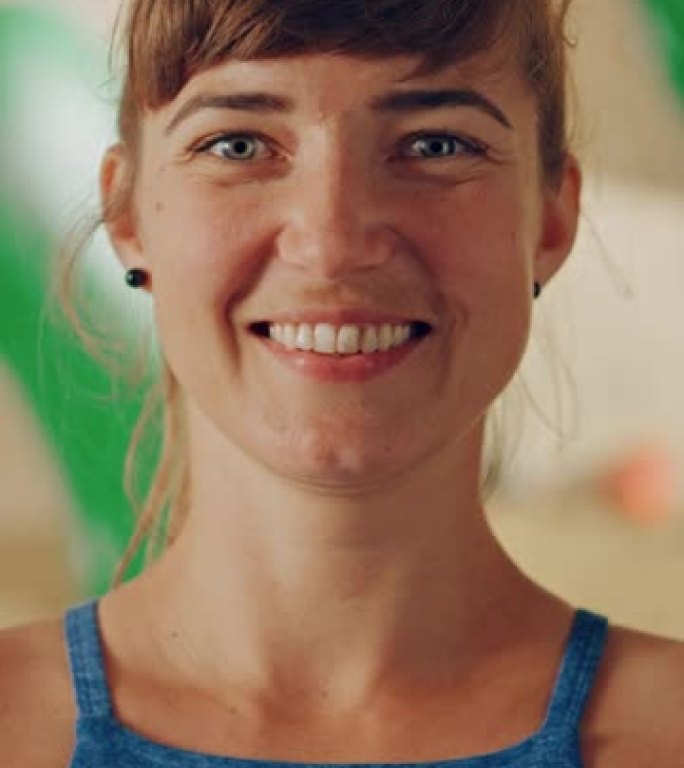 健康美丽的女运动员在攀岩馆微笑着摆姿势的垂直肖像，背景是抱石墙。迷人自信快乐的黑发女人做运动。健康的