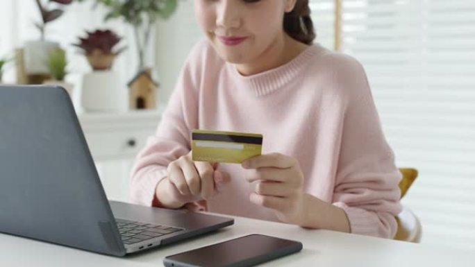 年轻的亚洲女人快乐支付网上购物用信用卡在家。