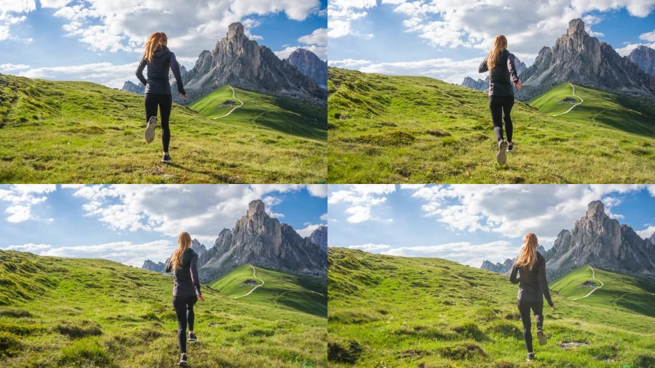 在阳光明媚的日子里，健康的女人在草地上奔跑，背景是雄伟的山脉