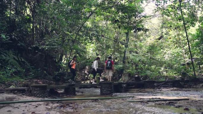3位亚洲华人朋友在森林中漫步穿越河上的桥梁丛林徒步旅行