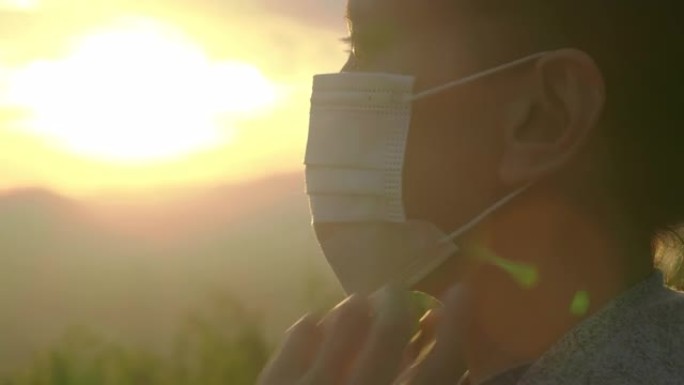 特写镜头，在日落背景时，年轻女性戴着防护口罩抵御空气污染，冠状病毒Covid19。口罩和面罩 (非高