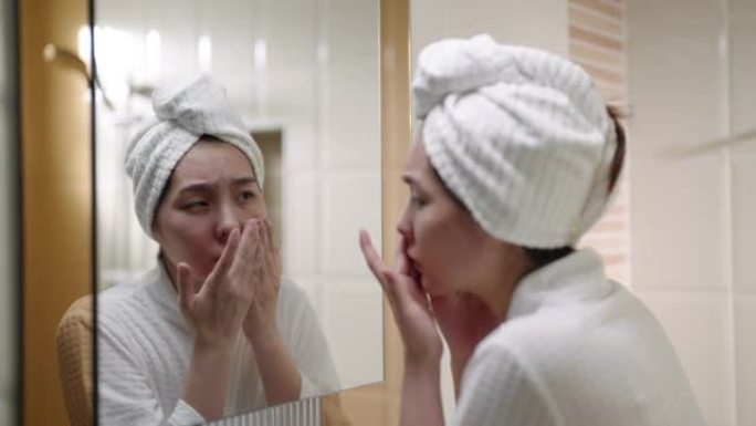 不满意的女人摸脸皮肤前浴室镜子