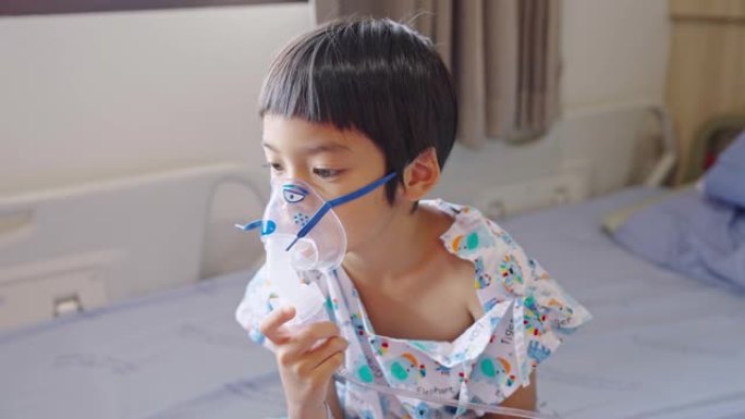 亚洲小男孩独自坐在医院的病床上，用吸入器呼吸，肺炎在医院康复。