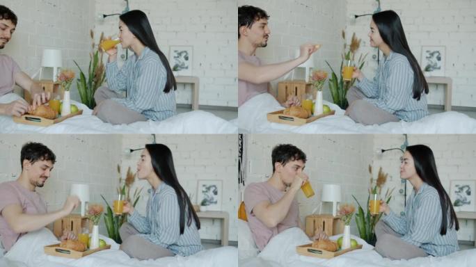 女孩和男孩在公寓的床上吃早餐，微笑着说话
