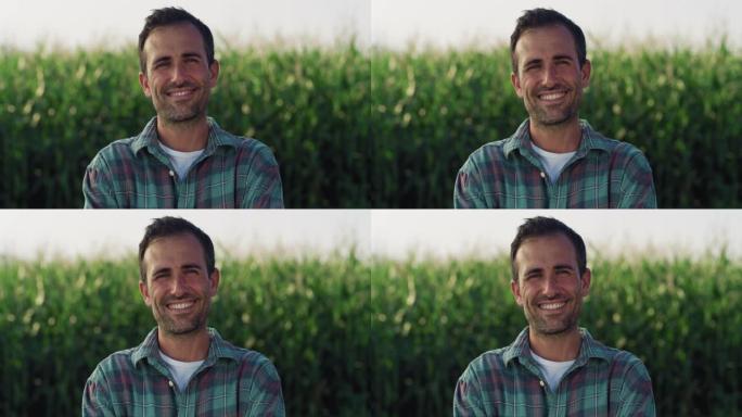 一个快乐的人的肖像在一片充满玉米作物的绿色田野里摆姿势，微笑着。英俊的中年男性农民看着镜头，享受着他