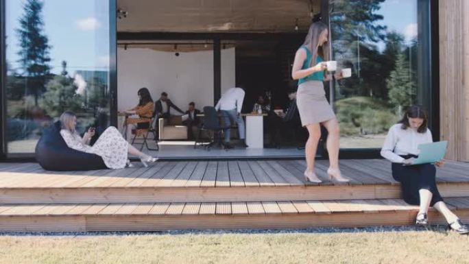 时尚的工作场所氛围。多元化的年轻商人坐在豆袋上，在办公室草地露台上喝咖啡