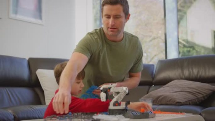 父亲和儿子穿着睡衣用塑料套件在家中建造机械臂，用于科学项目-慢动作拍摄