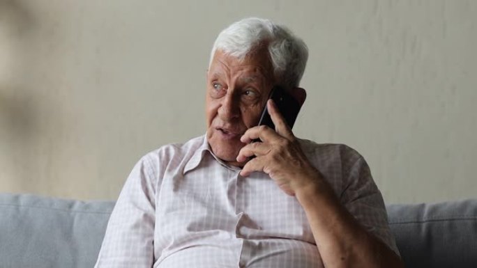 年长的男人坐在家里的沙发上用手机聊天