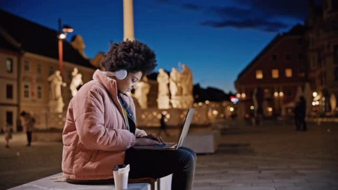 DS年轻女子晚上在城镇广场中央使用笔记本电脑