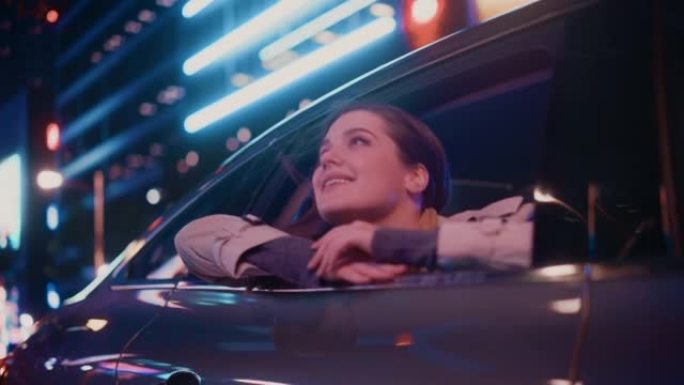 兴奋的年轻女性坐在汽车后座上，晚上通勤回家。看着窗外，惊讶地发现带有工作霓虹灯的城市街道多么美丽。电