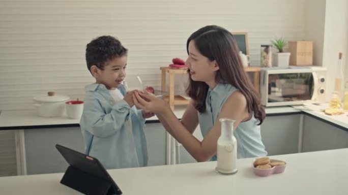 母亲将牛奶倒入玻璃杯中，供男孩在家吃早餐