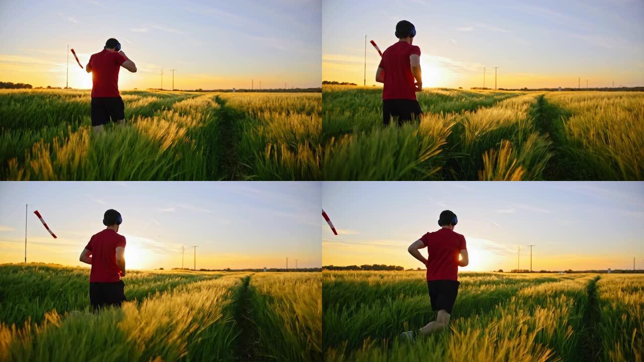 慢动作，跟踪男运动员在草地上开始跑步的镜头，播放音乐并奔向日落