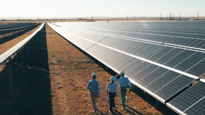 一组检查员正在成排的太阳能电池板之间行走。在太阳能发电厂工作的专业工程师。