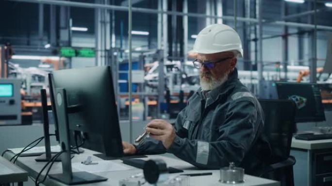 汽车厂办公室: 戴着安全安全帽在电脑上工作的男工程师的肖像。技术建筑构件。自动机械臂装配线制造电动汽