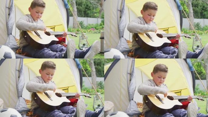 白人男孩坐在花园的帐篷里弹吉他