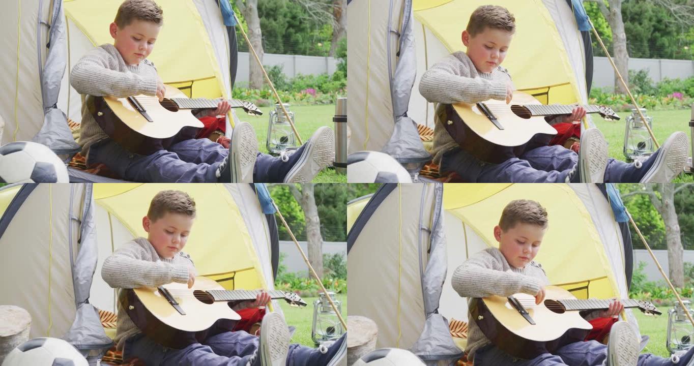 白人男孩坐在花园的帐篷里弹吉他