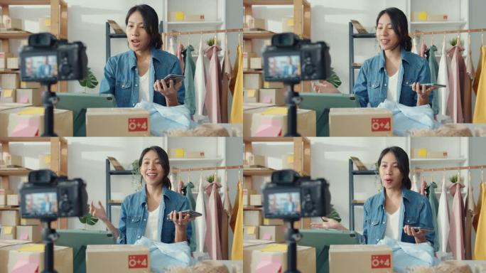 年轻的亚洲女士时装设计师使用手机接收订单，并在商店在线展示服装录制视频直播。