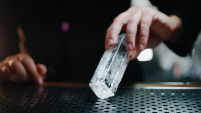 调酒师的特写镜头正在切割专业的水晶持久冰块，以便在酒吧或迪斯科俱乐部为顾客准备精英酒精鸡尾酒。