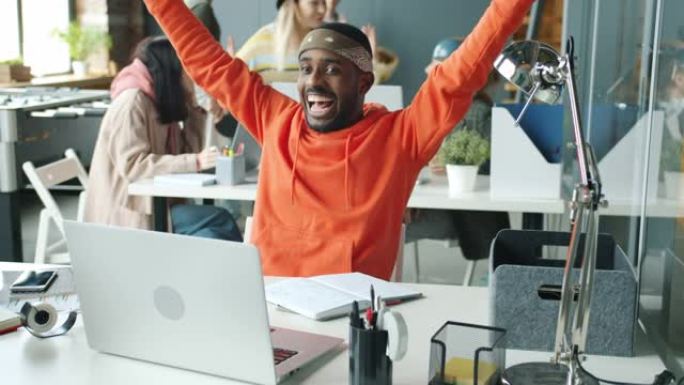 非洲裔美国企业家使用笔记本电脑，然后举起手臂，与同事一起享受击掌的好消息