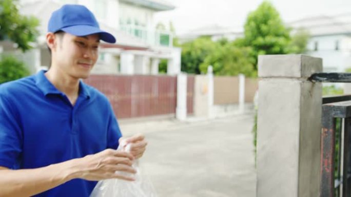 年轻的亚洲邮政快递快递员穿着蓝色衬衫处理食品盒，在家中发送给顾客，亚洲女性在户外接收包裹。