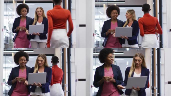 两名不同的女性办公室同事带着笔记本电脑在办公室散步时一起讨论