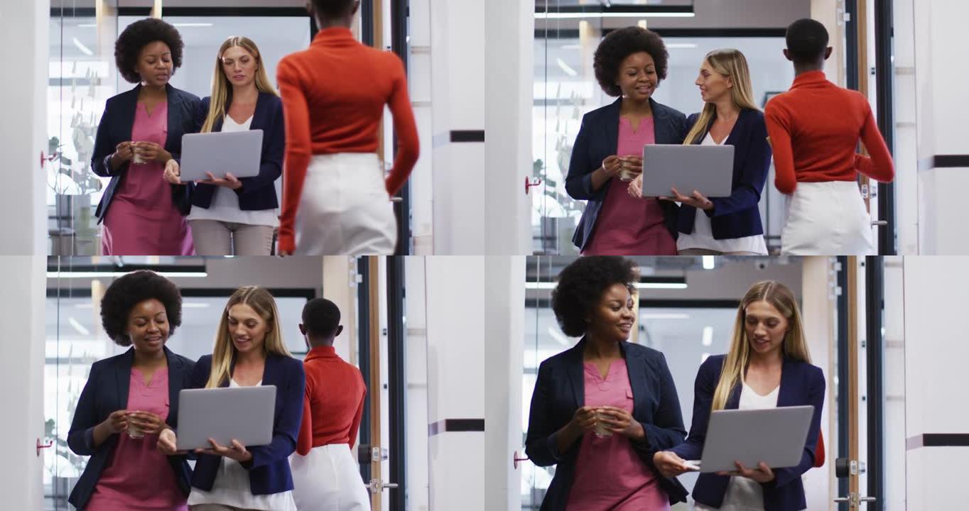 两名不同的女性办公室同事带着笔记本电脑在办公室散步时一起讨论