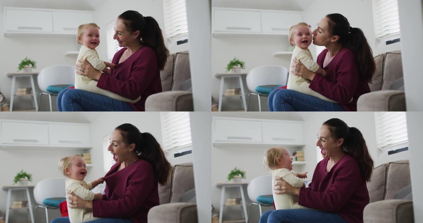 白人母亲坐在家里的沙发上与婴儿玩耍并亲吻她