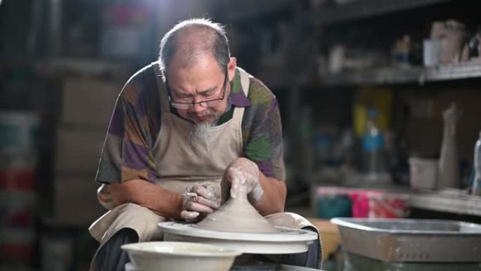 亚洲中国高级陶土艺术家在他的工作室里工作，用旋转的陶轮