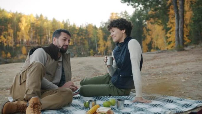 快乐的年轻夫妇享受户外野餐，在森林的格子上聊天放松