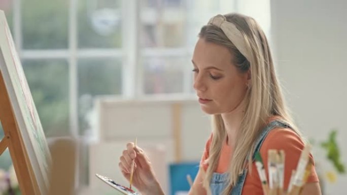 年轻的女画家在工作室里在画布上画彩画。严肃的艺术家使用画笔工具在车间画一朵花。创意女人画玫瑰的图像