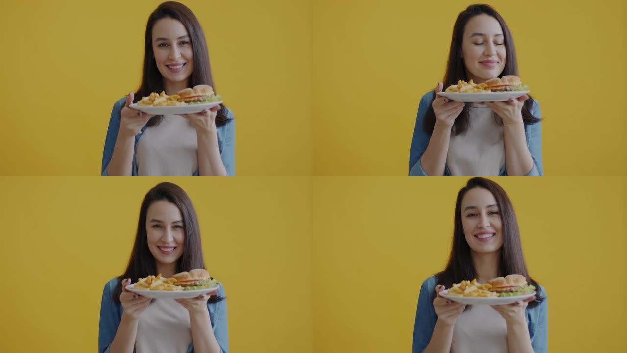 快乐的年轻女人的肖像闻到黄色背景上微笑着美味但不健康的食物