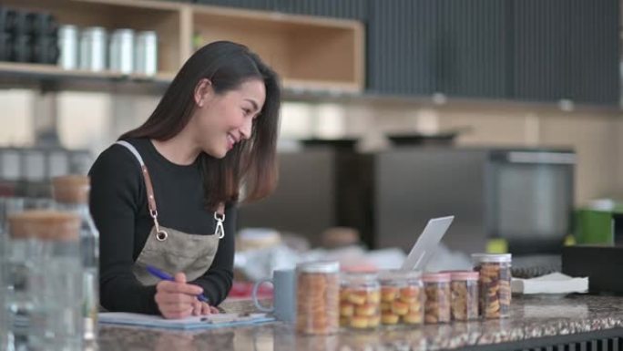 亚洲中国咖啡馆女老板在咖啡馆柜台用笔记本电脑围裙