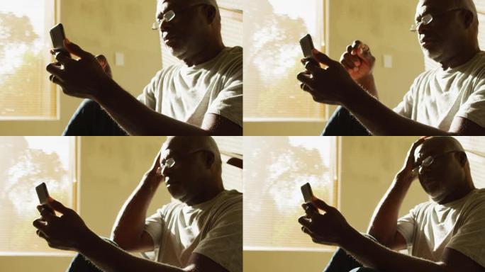 体贴的非洲裔美国老人坐在家里晒太阳，使用智能手机