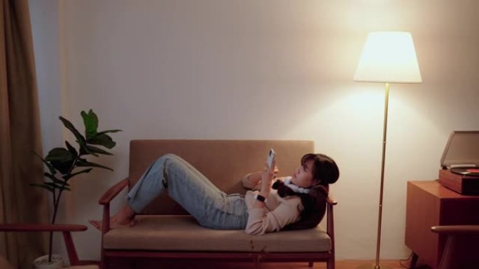 好看的亚洲女人躺在沙发上戴着耳机听音乐