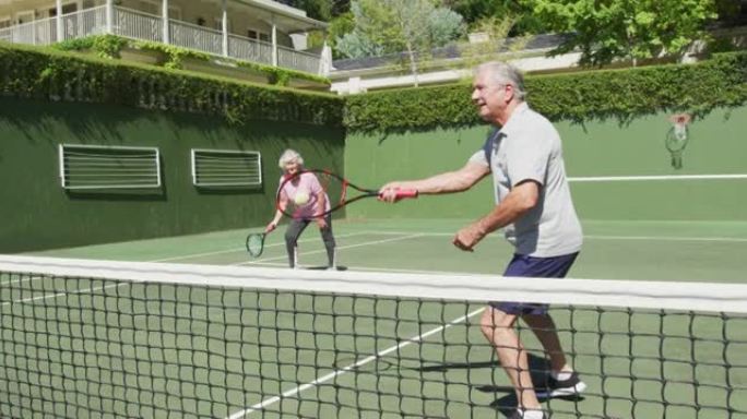 快乐的高加索高级夫妇在打了一场比赛后在室外网球场打双打