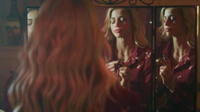 一位年轻迷人的性感女人穿着红色复古连衣裙，戴着金色长发，在家里的化妆间准备时，在镜子后面的嘴唇上涂上