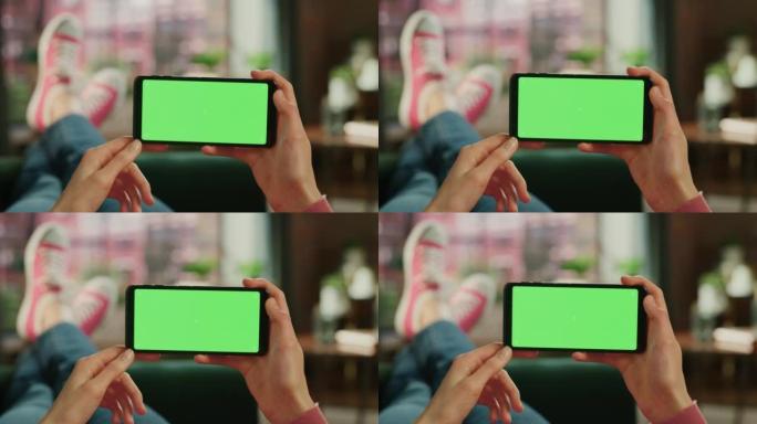 女人水平拿着智能手机，绿屏模拟显示。女性正在家里的沙发上放松，在移动设备上观看视频和阅读社交媒体帖子