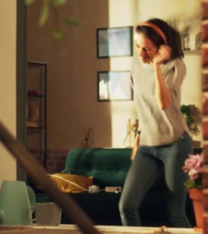 垂直屏幕: 快乐的西班牙裔妇女戴着无线耳机在舒适的公寓里跳舞。开朗活泼的女孩在家听音乐，心情愉快地跳