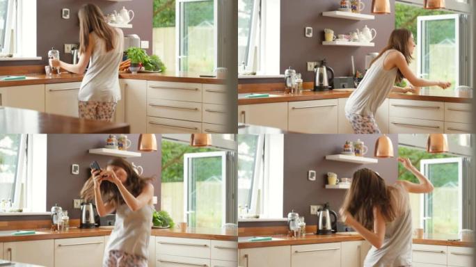 4k视频片段，一名年轻女子在厨房里跳舞，在智能手机上听音乐