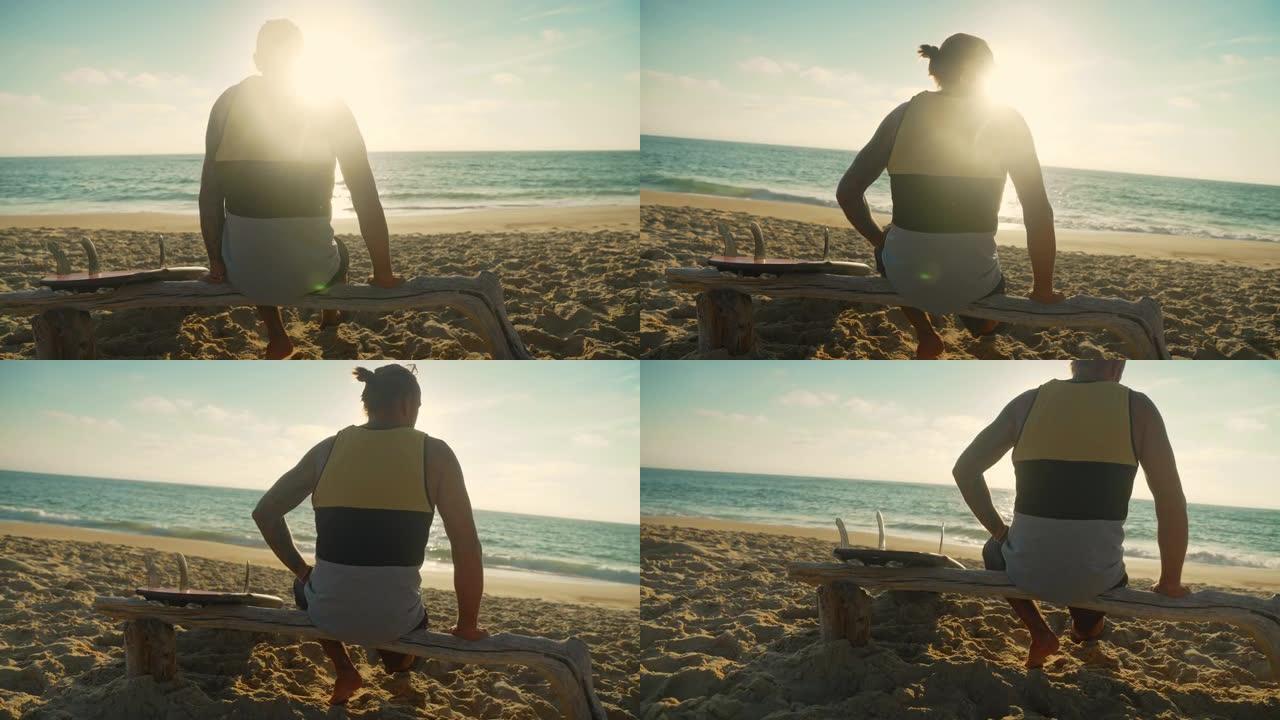 冲浪者坐在沙滩上看着海浪，冲浪板在他旁边，后视
