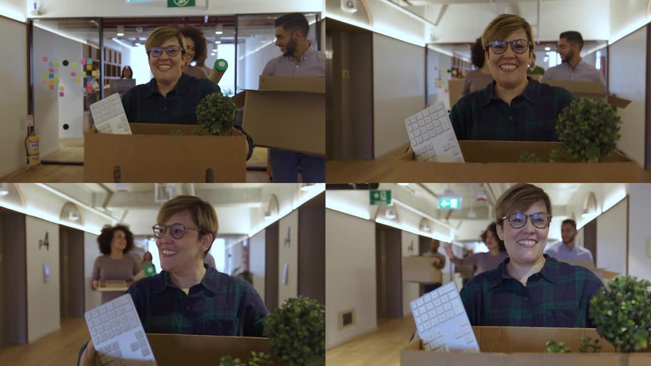 一群激动的员工搬进新办公室，一边拿着自己的物品一边微笑着