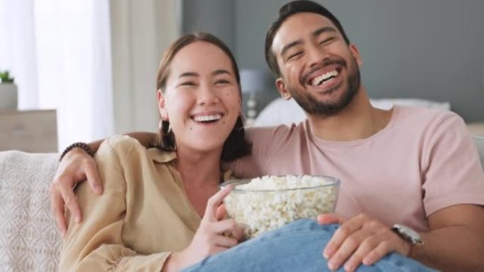 幸福的夫妻，在家里或房子的客厅里吃爆米花，看一部有趣的电影。爱情、浪漫和快乐的男人和女人在沙发上一起