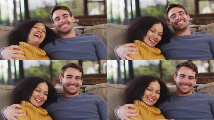 快乐的多元化夫妇坐在客厅的沙发上，拥抱和微笑的肖像