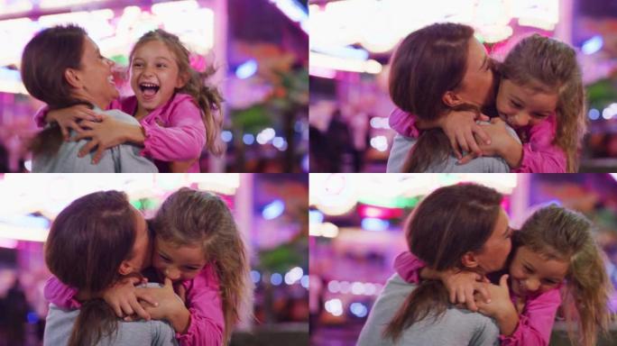 一个快乐微笑的女儿的真实镜头正在奔跑，给母亲一个情感的拥抱和亲吻，同时晚上在游乐园里与露娜公园的灯光